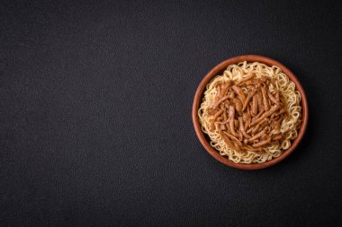 Lezzetli Asya mutfağı. İçinde pirinç, erişte, biber, mantar ve baharatlar var. Koyu beton arka planda.