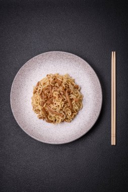 Lezzetli Asya mutfağı. İçinde pirinç, erişte, biber, mantar ve baharatlar var. Koyu beton arka planda.