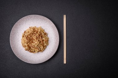 Lezzetli Asya mutfağı. İçinde pirinç, erişte, biber, mantar ve baharatlar var. Koyu beton arka planda.