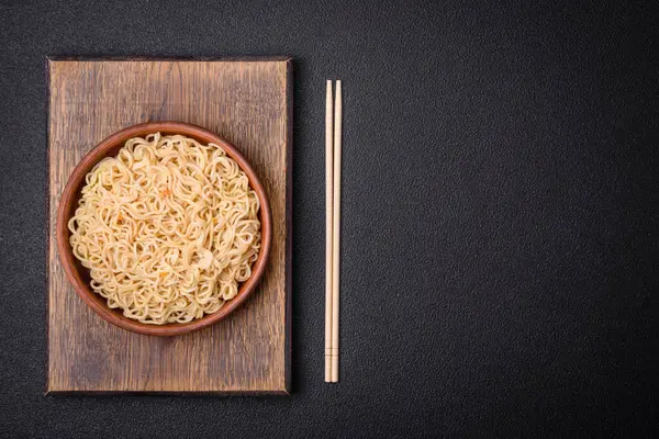 Lezzetli Asya mutfağı. İçinde pirinç, erişte, biber, mantar ve baharatlar var. Koyu beton arka planda.