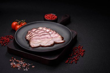 Lezzetli taze pancetta ya da tuzlu ve baharatlı pastırma koyu beton arka planda ince dilimler halinde kesilmiş.