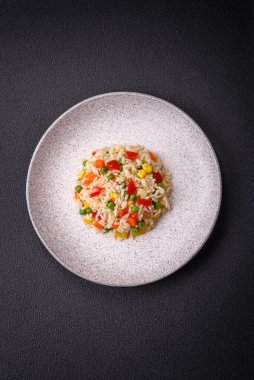 Lezzetli beyaz haşlanmış pirinç, sebzeli, tatlı biberli, havuçlu, bezelyeli, tuzlu ve baharatlı koyu beton arka planda.