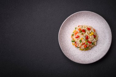 Lezzetli beyaz haşlanmış pirinç, sebzeli, tatlı biberli, havuçlu, bezelyeli, tuzlu ve baharatlı koyu beton arka planda.