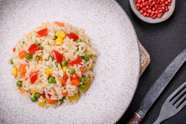 Lezzetli beyaz haşlanmış pirinç, sebzeli, tatlı biberli, havuçlu, bezelyeli, tuzlu ve baharatlı koyu beton arka planda.