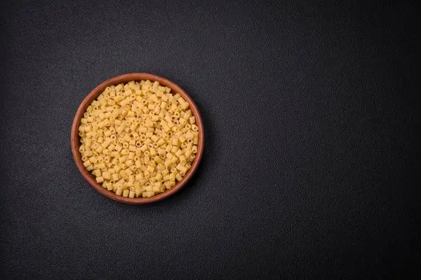 Ham ditali makarna, koyu beton arka planda buğdaydan yapılmış. Lezzetli, besleyici bir kahvaltı hazırlıyorum.