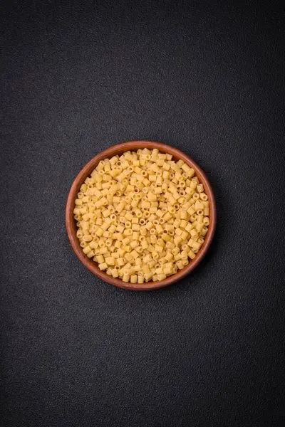 Ham ditali makarna, koyu beton arka planda buğdaydan yapılmış. Lezzetli, besleyici bir kahvaltı hazırlıyorum.