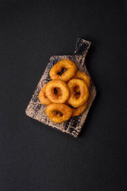 Lezzetli besleyici kalamar ya da soğan halkaları koyu beton arka planda tuz ve baharatla kızartılmış.