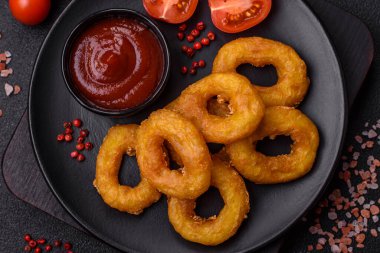 Lezzetli besleyici kalamar ya da soğan halkaları koyu beton arka planda tuz ve baharatla kızartılmış.