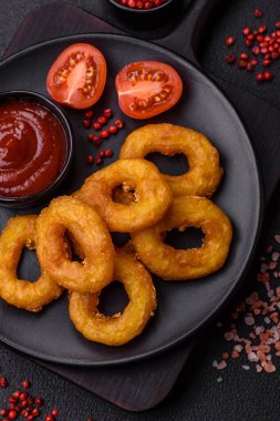 Lezzetli besleyici kalamar ya da soğan halkaları koyu beton arka planda tuz ve baharatla kızartılmış.