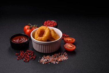 Lezzetli besleyici kalamar ya da soğan halkaları koyu beton arka planda tuz ve baharatla kızartılmış.