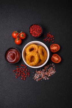 Lezzetli besleyici kalamar ya da soğan halkaları koyu beton arka planda tuz ve baharatla kızartılmış.