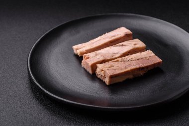 Lezzetli konserve ton balığı eti, tuz, baharat ve yağlı koyu beton arka planda.