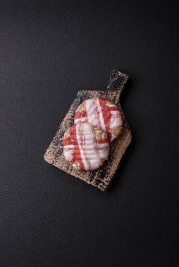 Koyu beton bir arka planda tuzlu, baharatlı ve otlu domuz pastırmasına sarılı yuvarlak doğranmış tavuk veya domuz pirzolası.