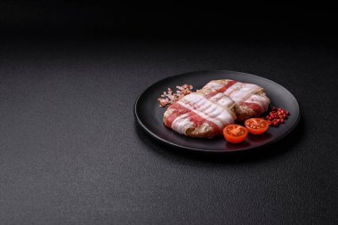 Koyu beton bir arka planda tuzlu, baharatlı ve otlu domuz pastırmasına sarılı yuvarlak doğranmış tavuk veya domuz pirzolası.