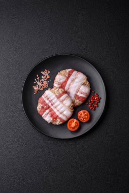 Koyu beton bir arka planda tuzlu, baharatlı ve otlu domuz pastırmasına sarılı yuvarlak doğranmış tavuk veya domuz pirzolası.