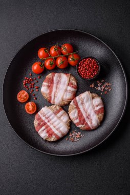 Koyu beton bir arka planda tuzlu, baharatlı ve otlu domuz pastırmasına sarılı yuvarlak doğranmış tavuk veya domuz pirzolası.