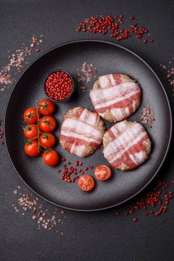 Koyu beton bir arka planda tuzlu, baharatlı ve otlu domuz pastırmasına sarılı yuvarlak doğranmış tavuk veya domuz pirzolası.