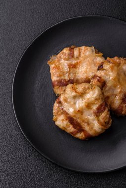 Koyu beton bir arka planda tuzlu, baharatlı ve otlu domuz pastırmasına sarılı yuvarlak doğranmış tavuk veya domuz pirzolası.