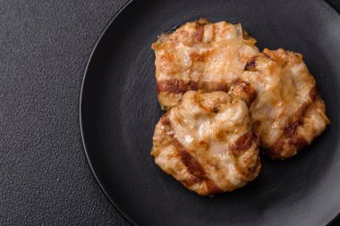 Koyu beton bir arka planda tuzlu, baharatlı ve otlu domuz pastırmasına sarılı yuvarlak doğranmış tavuk veya domuz pirzolası.