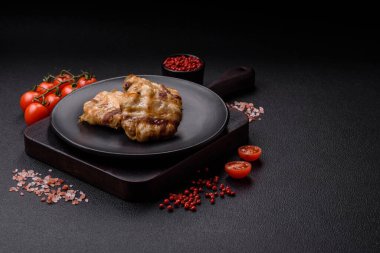 Koyu beton bir arka planda tuzlu, baharatlı ve otlu domuz pastırmasına sarılı yuvarlak doğranmış tavuk veya domuz pirzolası.