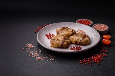 Koyu beton bir arka planda tuzlu, baharatlı ve otlu domuz pastırmasına sarılı yuvarlak doğranmış tavuk veya domuz pirzolası.