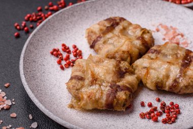Koyu beton bir arka planda tuzlu, baharatlı ve otlu domuz pastırmasına sarılı yuvarlak doğranmış tavuk veya domuz pirzolası.