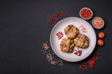 Koyu beton bir arka planda tuzlu, baharatlı ve otlu domuz pastırmasına sarılı yuvarlak doğranmış tavuk veya domuz pirzolası.