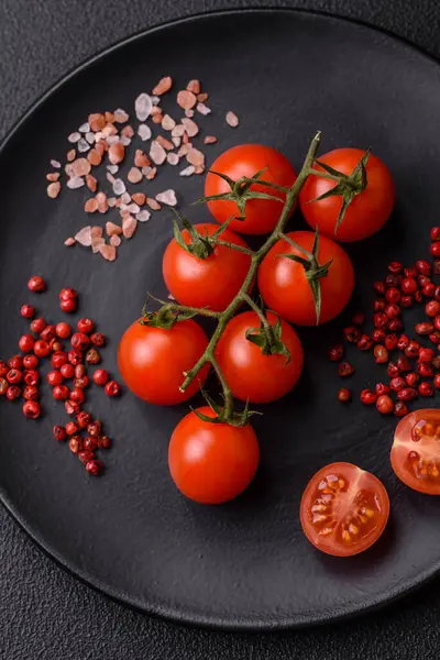 A branch of raw cherry tomatoes with salt and spices on a dark background. Ingredients for cooking at home