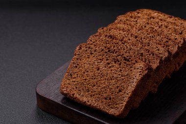 Tohumları ve tahılları olan lezzetli kahverengi ekmek desenli beton bir arka planda dilimler halinde kesilmiş.