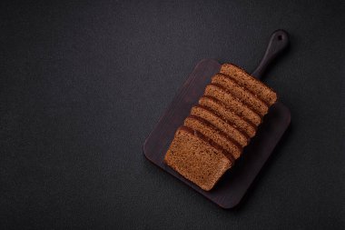 Tohumları ve tahılları olan lezzetli kahverengi ekmek desenli beton bir arka planda dilimler halinde kesilmiş.