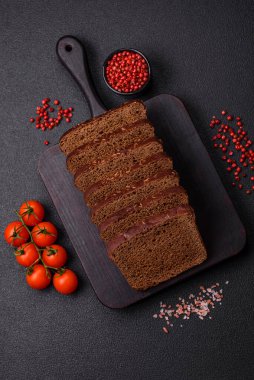 Tohumları ve tahılları olan lezzetli kahverengi ekmek desenli beton bir arka planda dilimler halinde kesilmiş.