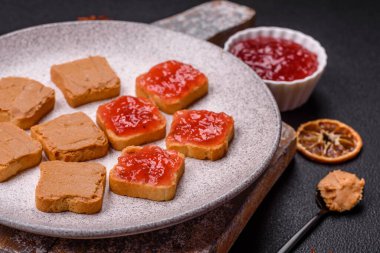 Fıstık ezmeli lezzetli, besleyici sandviçler, koyu beton arka planda çilek reçeli.