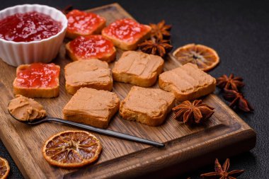 Fıstık ezmeli lezzetli, besleyici sandviçler, koyu beton arka planda çilek reçeli.