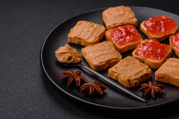 Fıstık ezmeli lezzetli, besleyici sandviçler, koyu beton arka planda çilek reçeli.