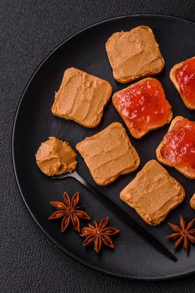 Fıstık ezmeli lezzetli, besleyici sandviçler, koyu beton arka planda çilek reçeli.