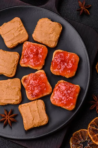 Fıstık ezmeli lezzetli, besleyici sandviçler, koyu beton arka planda çilek reçeli.