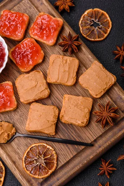 Fıstık ezmeli lezzetli, besleyici sandviçler, koyu beton arka planda çilek reçeli.