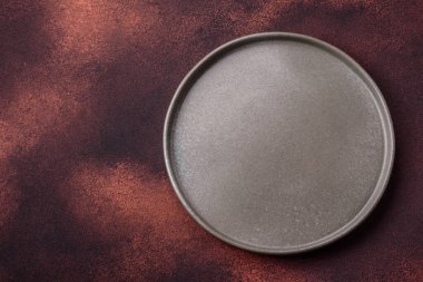 Empty ceramic round plate on dark textured concrete background. Cutlery, preparation for dinner