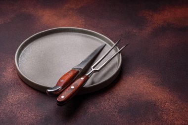 Empty ceramic round plate on dark textured concrete background. Cutlery, preparation for dinner
