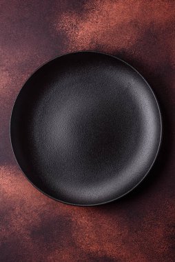 Empty ceramic round plate on dark textured concrete background. Cutlery, preparation for dinner