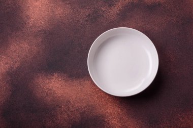 Empty ceramic round plate on dark textured concrete background. Cutlery, preparation for dinner