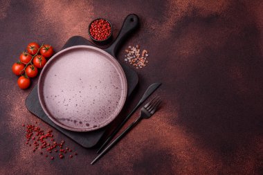 Empty ceramic round plate on dark textured concrete background. Cutlery, preparation for dinner