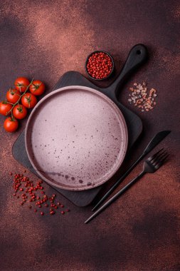 Empty ceramic round plate on dark textured concrete background. Cutlery, preparation for dinner