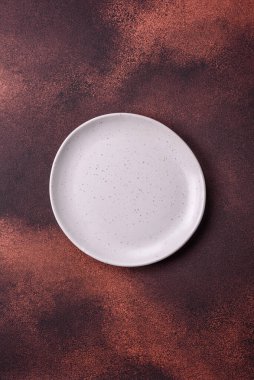 Empty ceramic round plate on dark textured concrete background. Cutlery, preparation for dinner