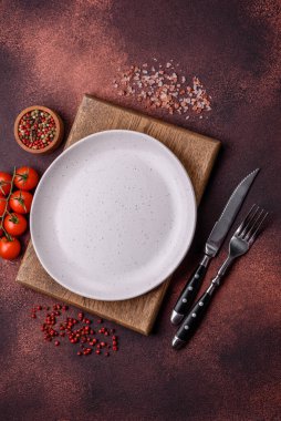 Empty ceramic round plate on dark textured concrete background. Cutlery, preparation for dinner