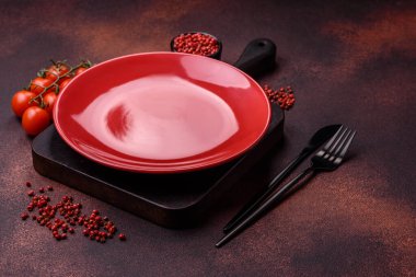 Empty ceramic round plate on dark textured concrete background. Cutlery, preparation for dinner