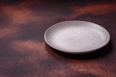 Empty ceramic round plate on dark textured concrete background. Cutlery, preparation for dinner
