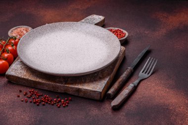 Empty ceramic round plate on dark textured concrete background. Cutlery, preparation for dinner