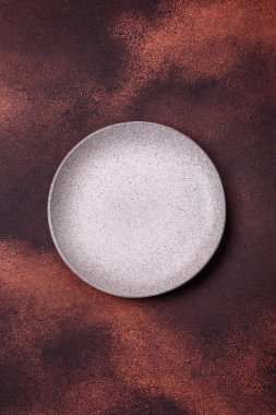 Empty ceramic round plate on dark textured concrete background. Cutlery, preparation for dinner
