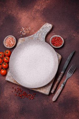 Empty ceramic round plate on dark textured concrete background. Cutlery, preparation for dinner